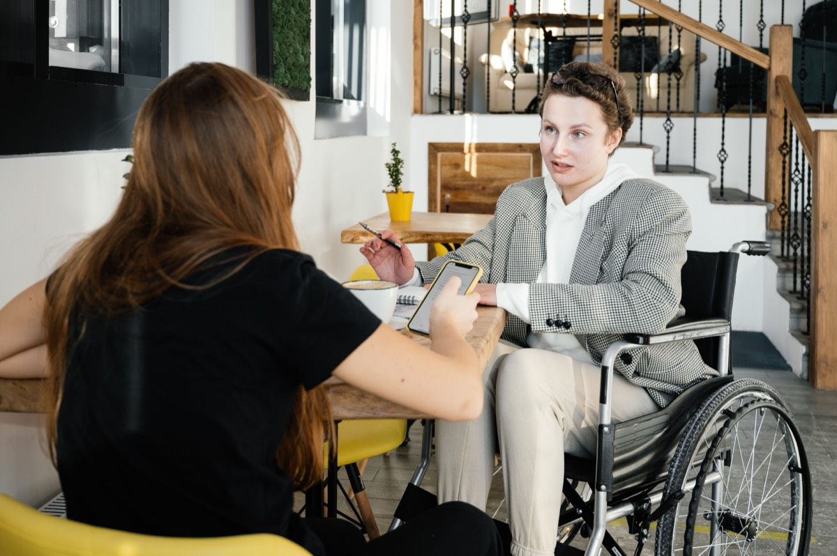 A man using a wheelchair talking with a support professional across a table.