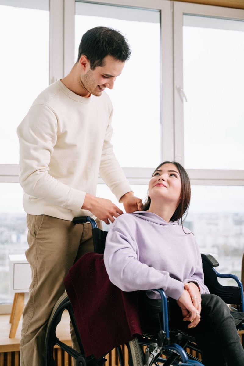 A support worker helping a young woman who uses a wheelchair, in a bright room at home.