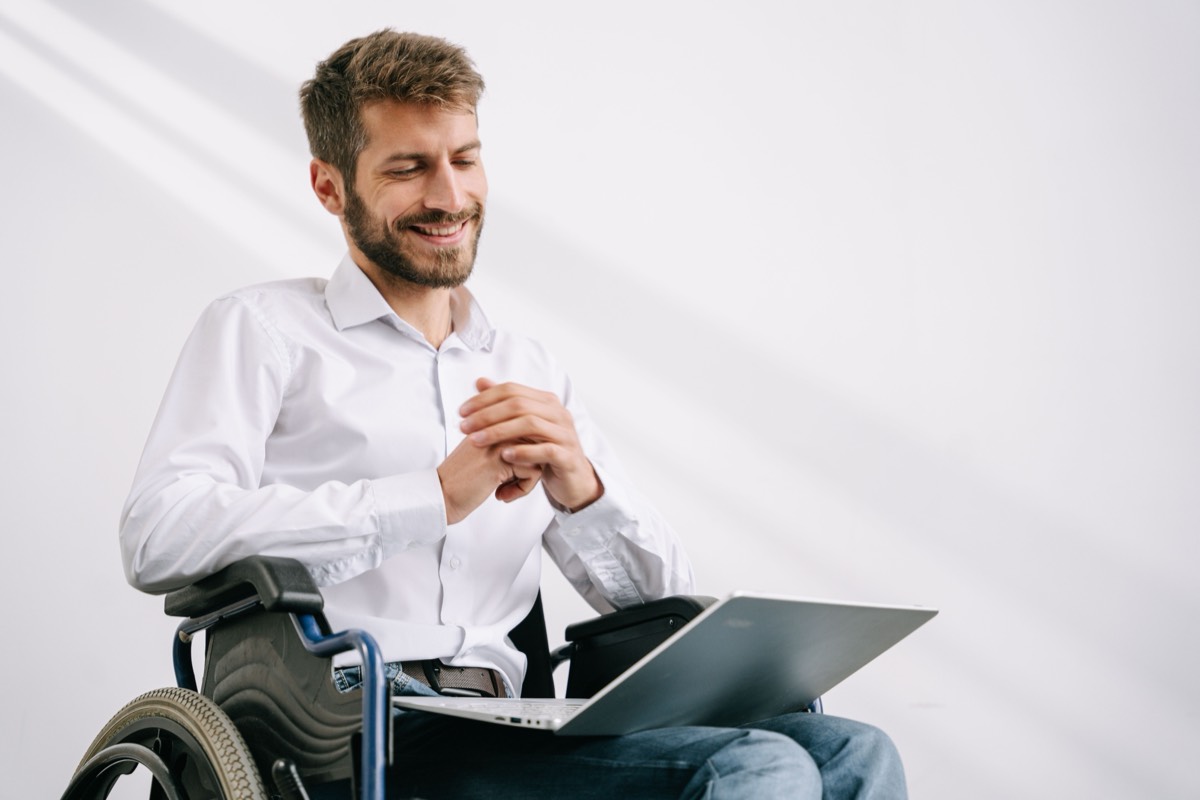 A man using a wheelchair working at a laptop, smiling.